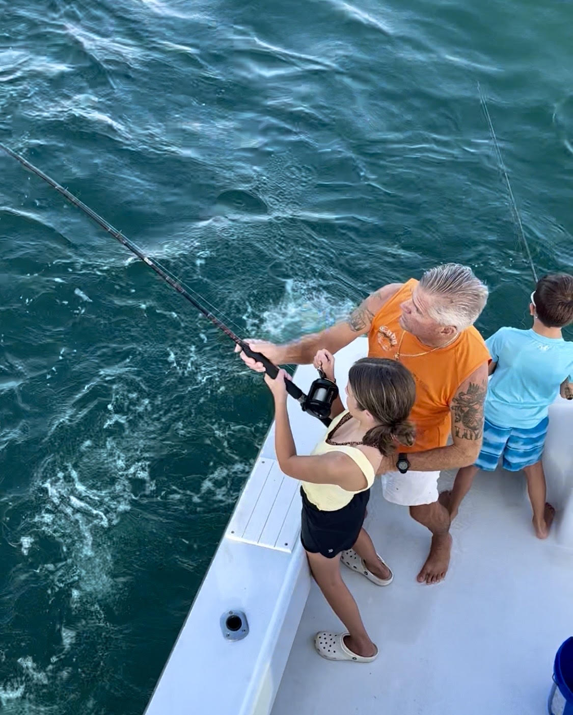 Captain Tino helping a family reel in a fish on the deck of The Shark
